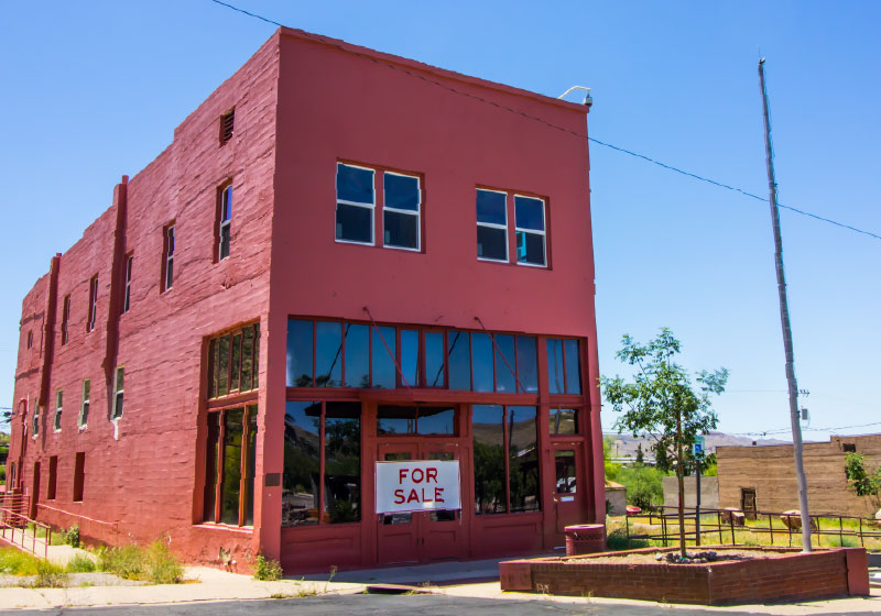 Red warehouse has a for sale sign in its front window.