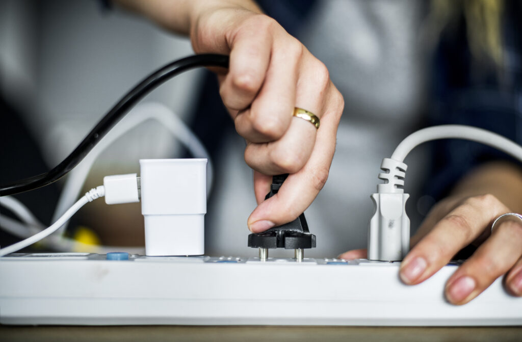 A man is plugging a device into a powerstrip which displays a fire hazard that could be detected through thermal imaging.