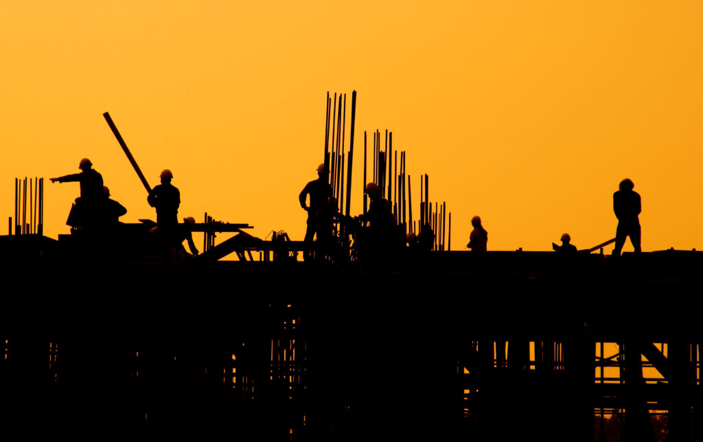 A construction crew works on a new property against a yellow backdrop, symbolizing the importance of draw inspections